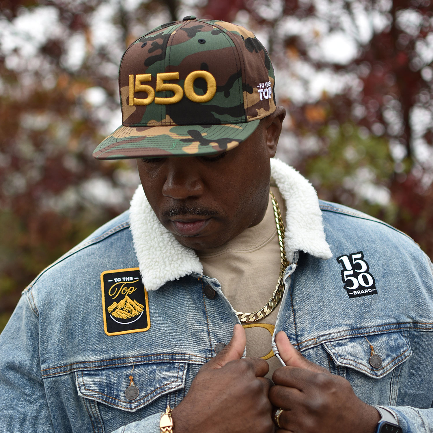 Black man wearing 1550 Brand denim jacket, 3D puff embroidered logo hat, and To the Top patch designed by Blue Agate Creative